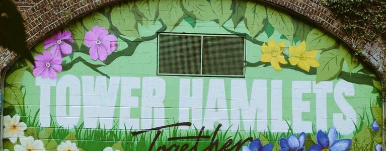 A mural of flowers and shades of green, painted on the wall under a railway arch. Text reads ‘Tower Hamlets Together’.