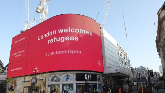 Piccadilly Circus screen saying London welcomes refugees on a pink background
