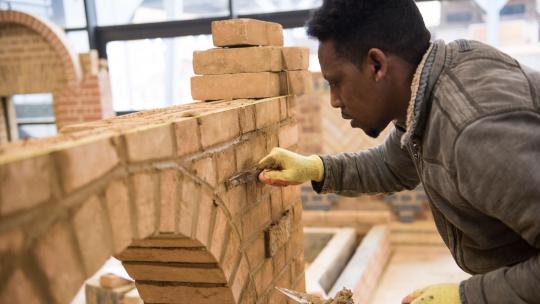 Man learning how to build an arch with bricks