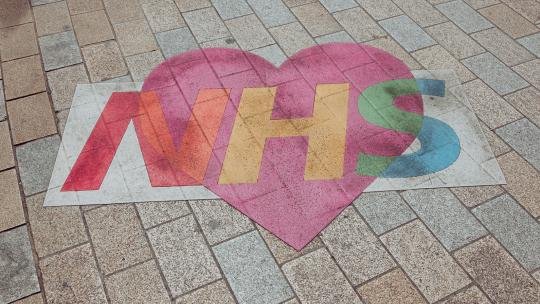 the NHS logo on a heart shaped sign on brick surface