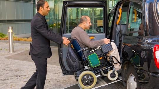 Porter pushing guest in wheelchair into accessible taxi