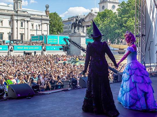 West End Live performers in costume on stage with large crowd watching