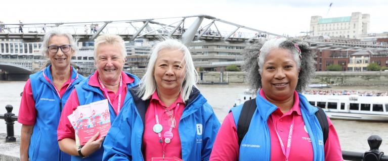Four Team London Ambassadors volunteers posing for picture in front of River Thames and holding Let's Do London campaign leaflets