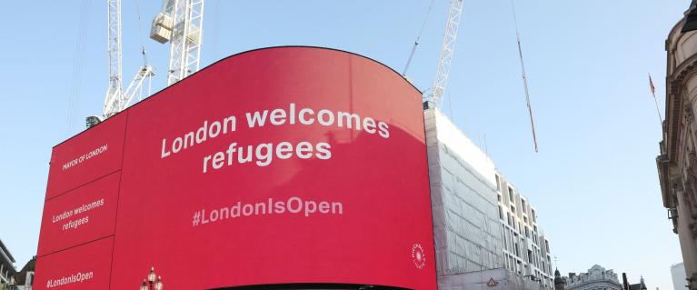 Piccadilly Circus screen saying London welcomes refugees on a pink background
