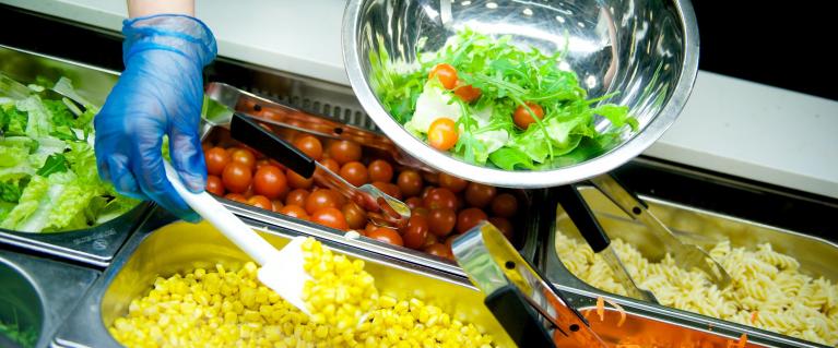 A bowl being filled with fresh salad.