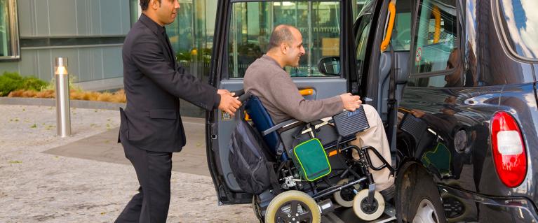 Porter pushing guest in wheelchair into accessible taxi