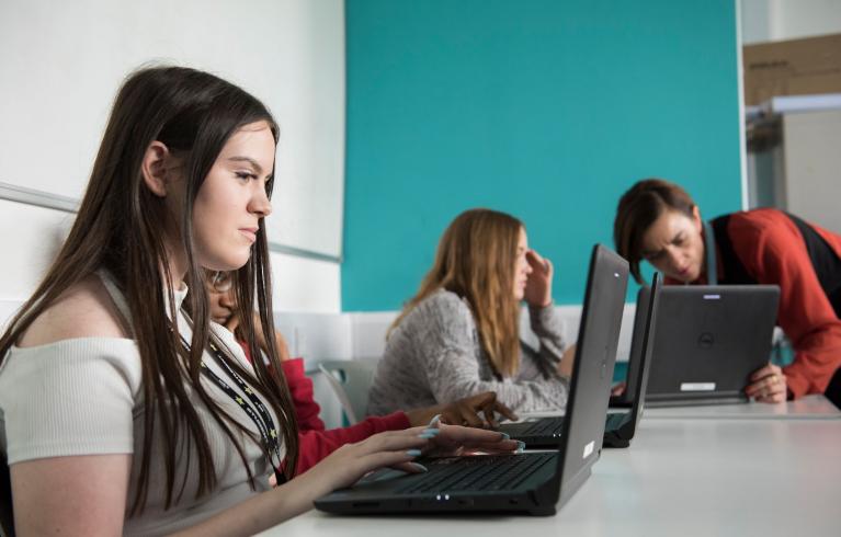 Three young people and teacher looking at information on laptops