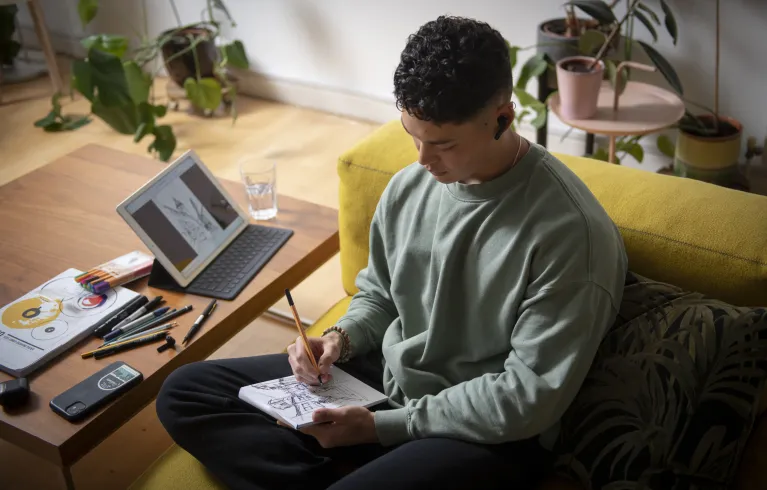 Young man following online tutorial and drawing on a notepad