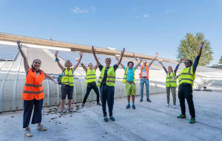 A group of people in hi-vis vests with their hands raised