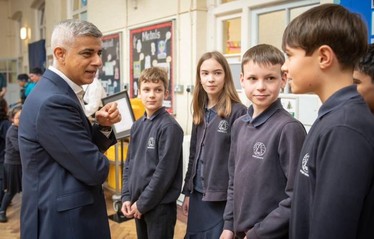Mayor of London, Sadiq Khan, standing with students in a school dinner hall.