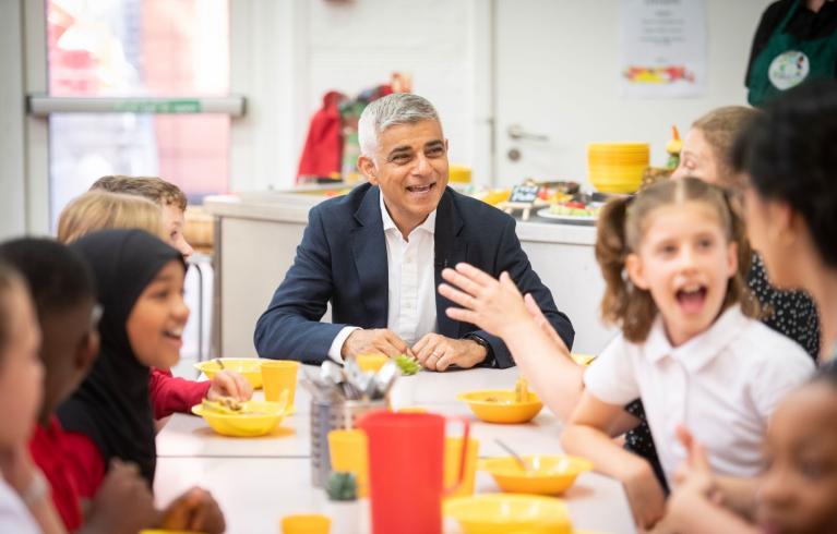 The Mayor of London Sadiq Khan with school students seated around a table with school meals.