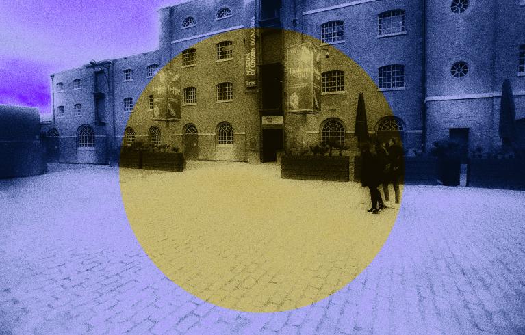 London Docklands public square photograph with a faded, grainy purple filter overlaid. A central yellow circle spotlights the location for a new memorial artwork.