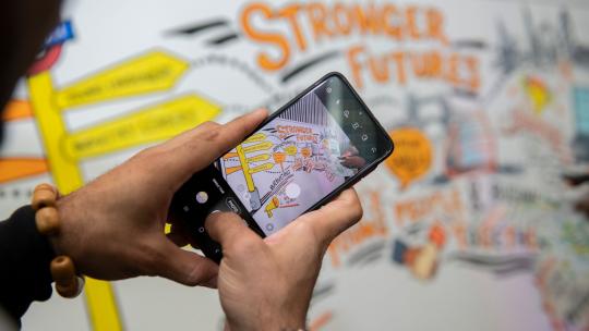 Young person taking picture of Stronger Future board with mobile phone