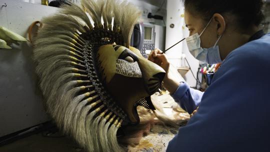 A person with a paint brush in their hand, brushing a lion head piece from Disney's The Lion King theatre