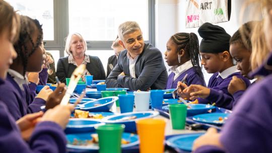 Sadiq Khan sits at a lunch table and talks with pupils in a primary school 