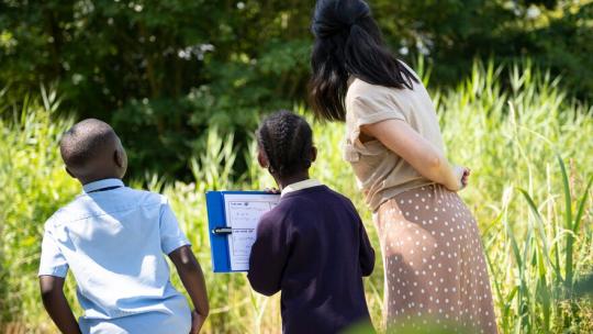 Image of a teacher and two student looking at a field 