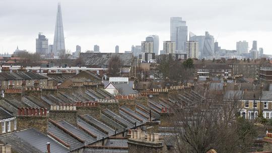 Rooftops of terraced houses in London with London's skyline in the horizon.