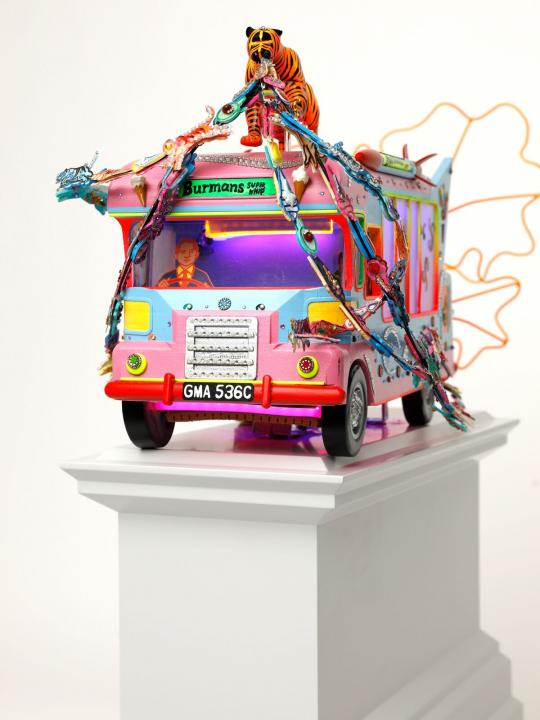 Close up side angle view of blue and pink tone ice cream van with a tiger on top with jewels streaming out of its mouth on a light grey plinth