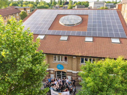 A photo of community members holding up a banner outside a community centre with solar panels installation.
