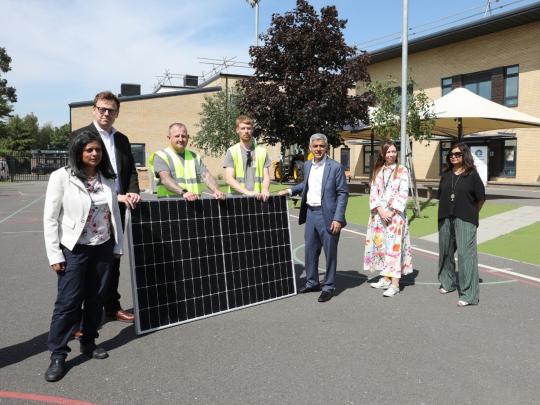 The Mayor of London, Sadiq Khan, standing beside solar panels with members of public.