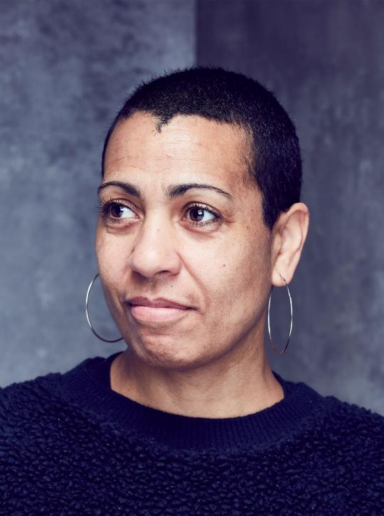 A headshot of the artist Helen Cammock, who is mixed race and has short dark hair. She is wearing silver hooped earrings