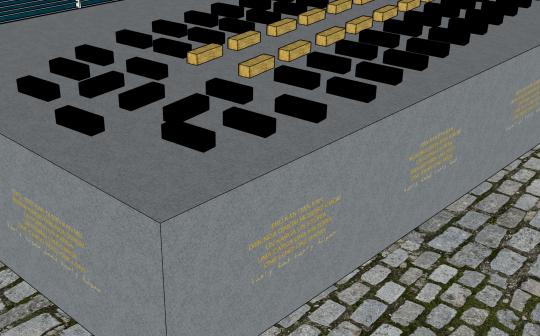 Close up of large grey, solid block, with gold coloured text in different languages, around the side of the and on top of the grey block are smaller black blocks and a few gold coloured blocks. 