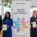 Six people of different ages stand next to a large banner at action plan launch event. The banner reads "Making London age friendly". 
