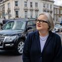 Caroline Russell, standing in front of moving traffic at a London street corner, looks pensively off to the lefthand side of the frame without smiling.