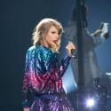 Taylor Swift holding a mic and wearing a shinny jacket 