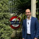 Assembly Member Bassam Mahfouz standing in front of the Eastcote TfL roundel sign, with plants and greenery surrounding him 