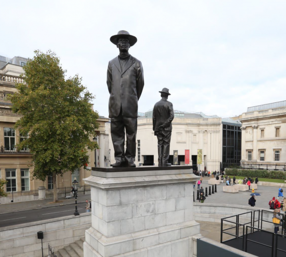 A bronze statue of two men wearing hats on the fourth plinth of Trafalgar Square by Samson Kambalu