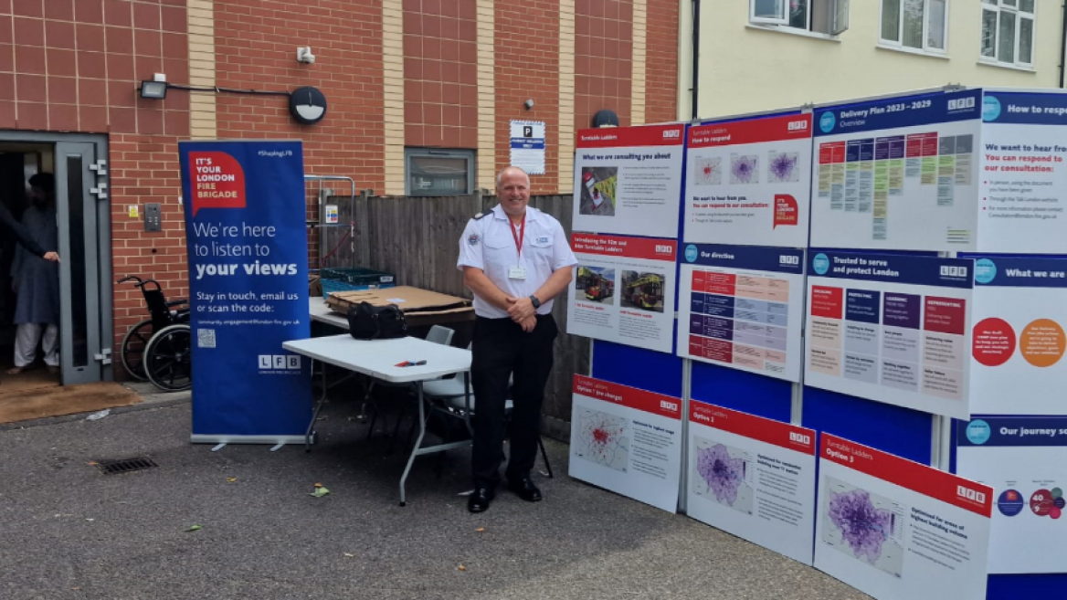 A London Fire Brigade firefighter standing in front of a banner about the 'Your Fire Brigade' strategy and delivery plan